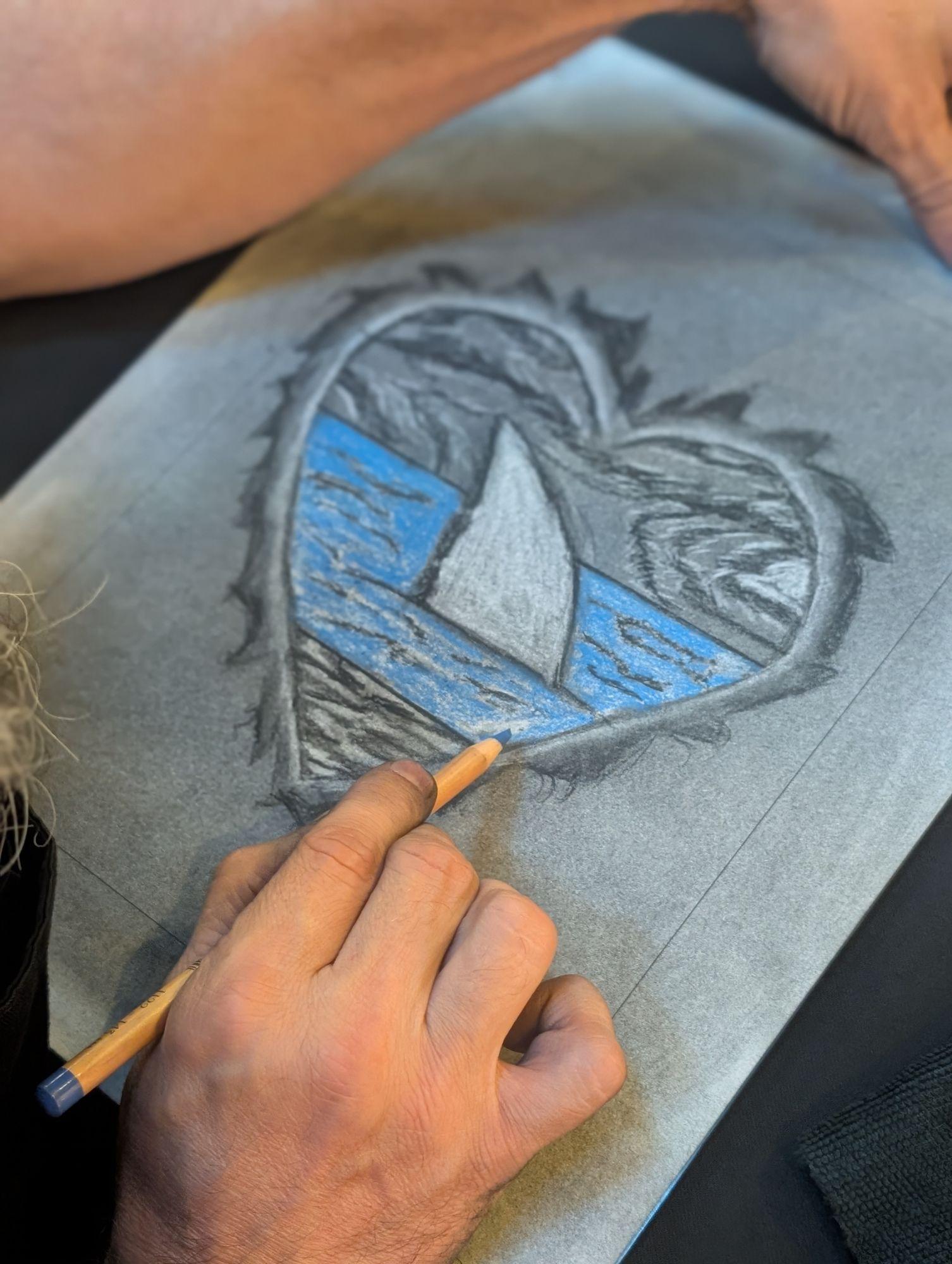 A hand adding a blue charcoal detail to a drawing
